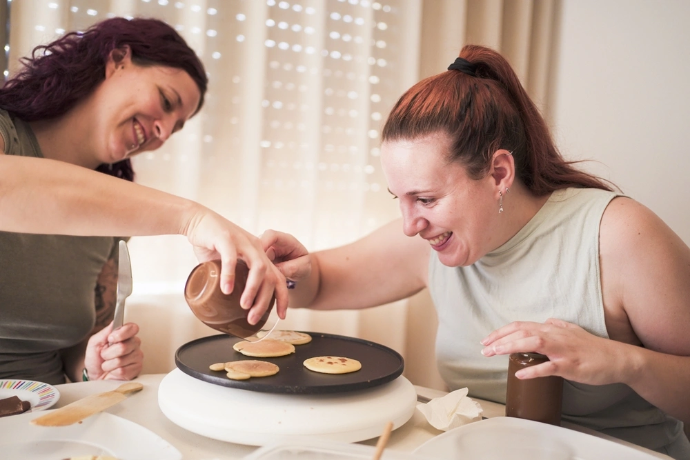 women helping a disabled friend with cooking panckakes